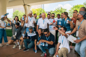 A group of people wearing ID badges and lanyards, some holding drinks, gather together outdoors, smiling and posing for a photo under an interstate overpass. They're attending Vondace Contracting's 60th anniversary party at City Walk BHAM.