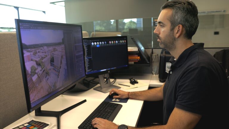 A person sits at a desk in an office, working on dual monitors. One screen displays a 3D rendering of a construction project, while the other shows software tools, embodying the dynamic opportunities found in Vondace Contracting careers.