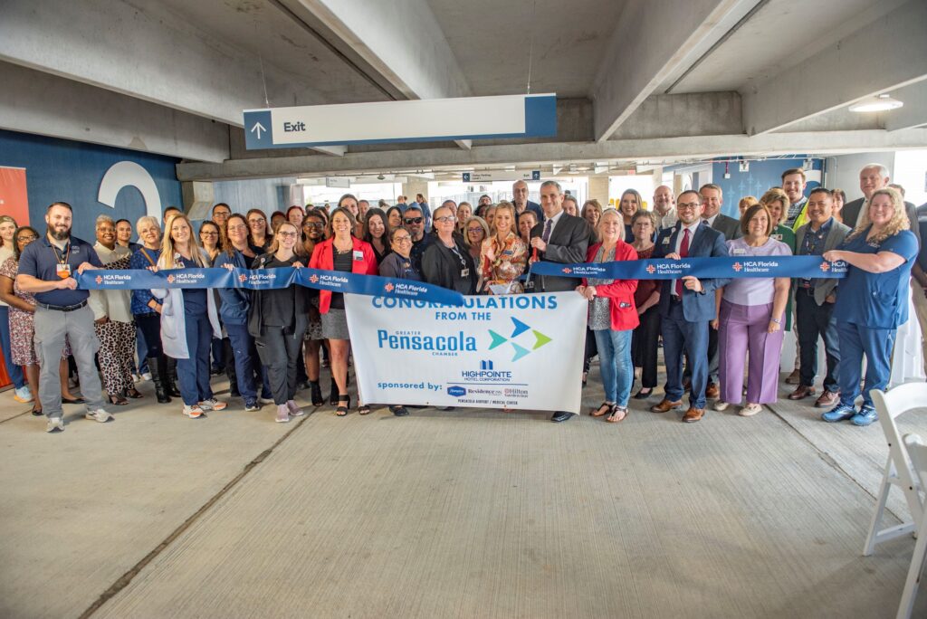 At a ribbon-cutting ceremony for the new parking garage construction, a group proudly holds a banner proclaiming "Congratulations from the Pensacola" with logos from the Greater Pensacola Chamber, Highpointe Hotel Corporation, Hampton by Hilton, Residence Inn by Mariott, Hilton Garden Inn and Pensacola Airport/Medical Center lined up neatly at the bottom.