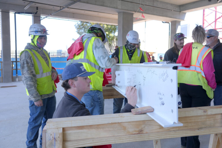 Construction workers, clad in safety gear, sign a large white beam at the site of the new Center of Hope for the Salvation Army in Metro Atlanta.