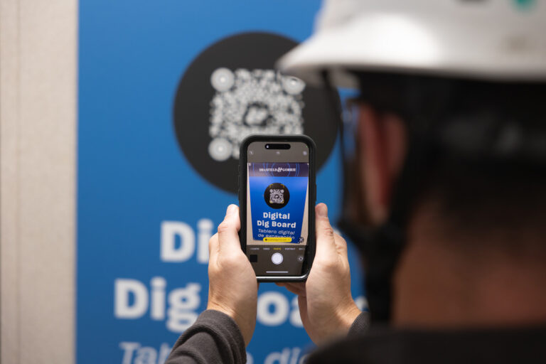 A person wearing a white safety helmet scans a QR code on the wall with their smartphone, revealing a 