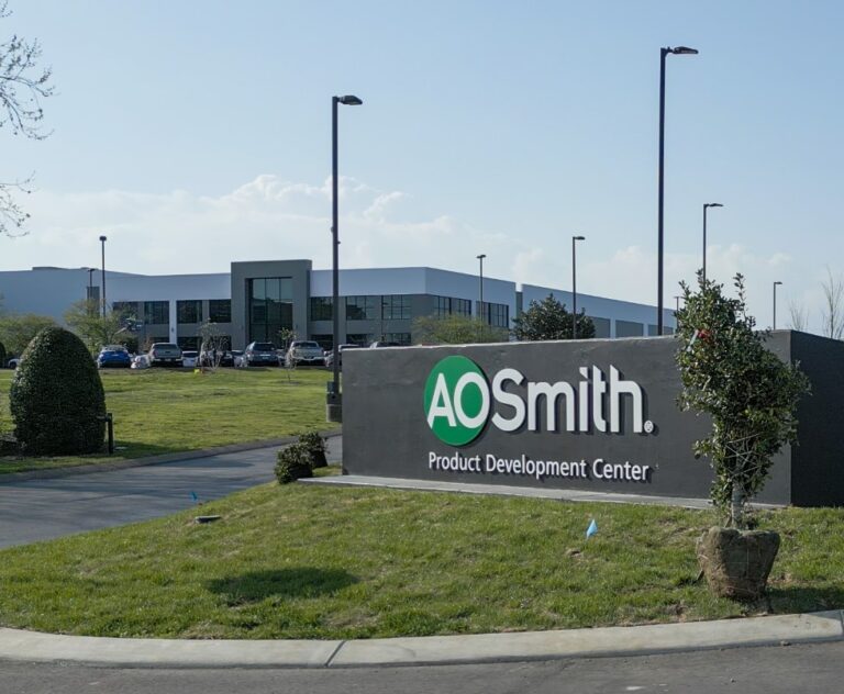 A. O. Smith Product Development Center exterior with company sign, modern new building, parked cars, and landscaped lawn under a clear sky.