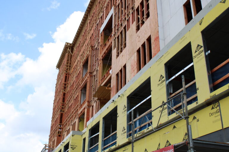 Multi-story building under construction on North Graham Street in Charlotte, featuring exposed wooden framing and yellow insulation panels on the lower floors.