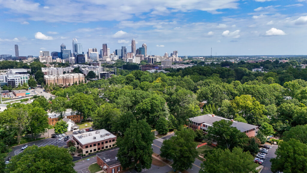 A brick building at a construction milestone, with a partially constructed balcony and equipment in front, surrounded by trees and parked cars—part of the Ronald McDonald House Greater Charlotte project.