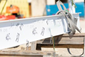 A white steel beam with "Vondace Contracting" and a Texas outline logo, signed by various people, rests on wooden supports at a construction site.