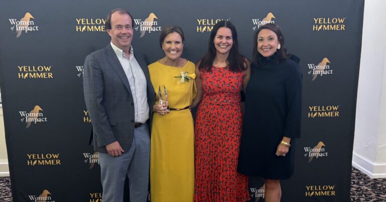 Four people stand together smiling in front of a 