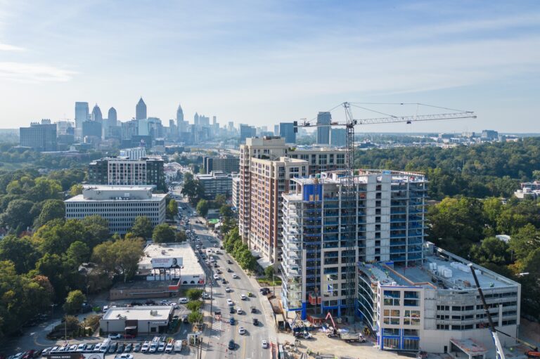 Aerial view of a city with a high-rise building under construction by Vondace Contracting, a crane at work, busy streets below, and a skyline of tall buildings in the distance.