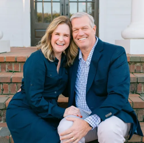 A smiling couple sits together on brick steps in front of a building with white columns.